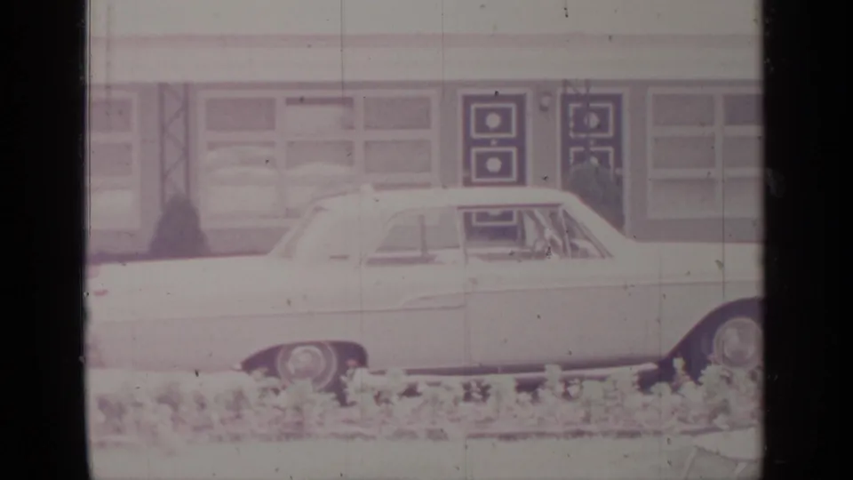Low-angle 8mm frame of the white sedan with its side panels and wheel visible below a row of building windows in Greenwood Lake.