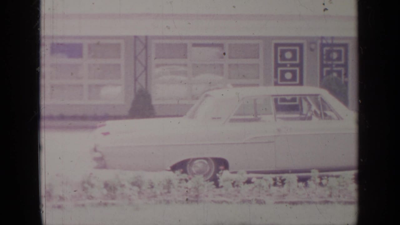 Light-colored sedan parked in front of a building with large windows and patterned doors.