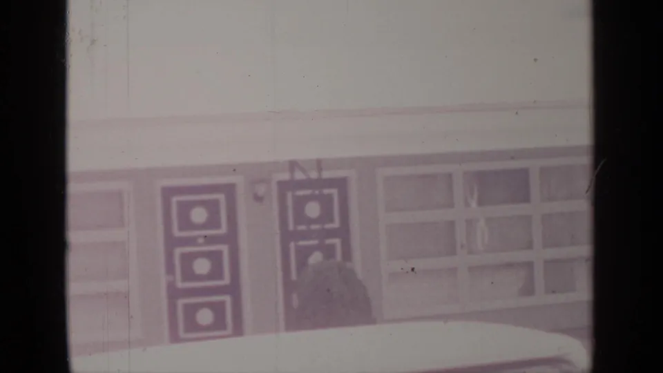 Final Greenwood Lake frame showing geometric double doors, a wide window section, shrubs, a pale foreground, and visible 8mm film wear.