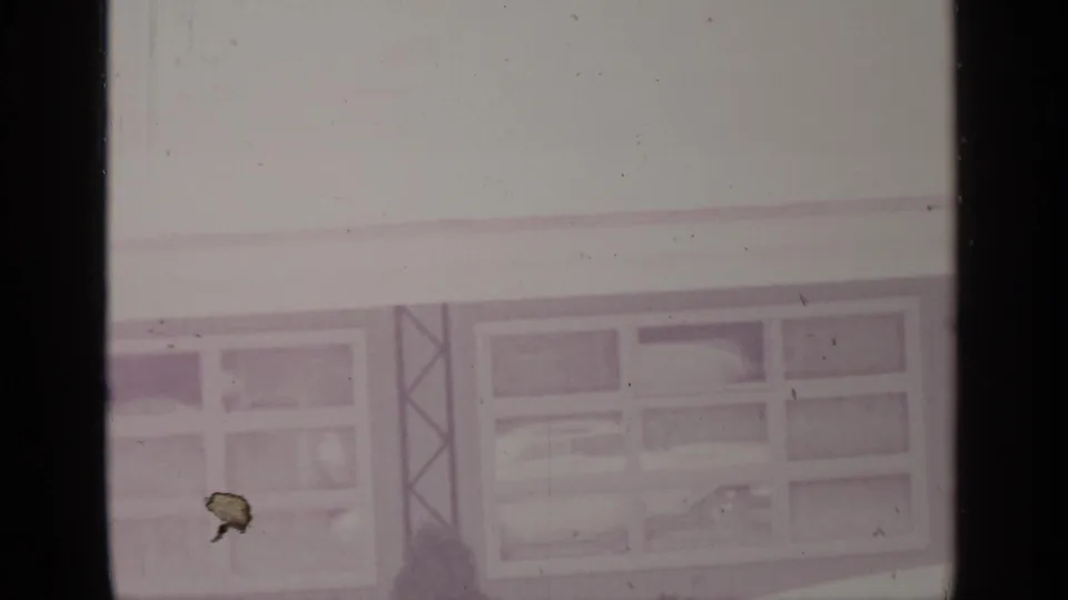 1964 home-movie frame of a snowy Greenwood Lake building exterior with broad windows and a vertical support detail.