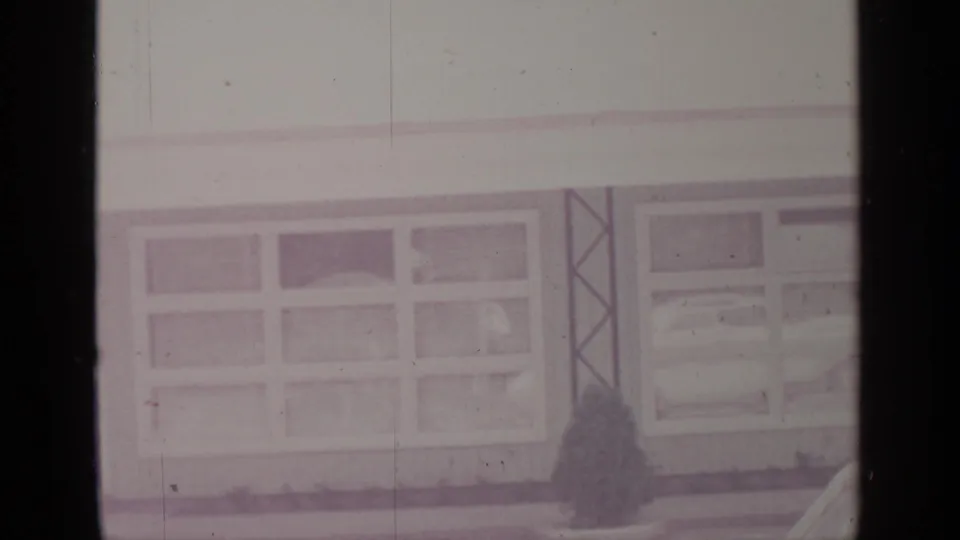 End of the pan across a 1964 Greenwood Lake winter building exterior with windows, snow, and a small dark shrub near the wall.