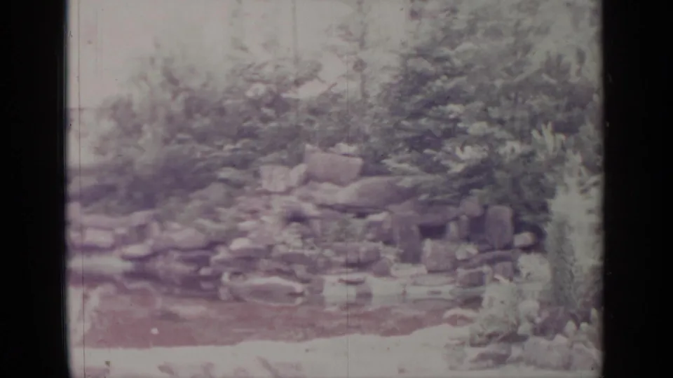 Greenwood Lake 1964 frame showing a quiet residential rock garden, shrubs, and a small wet or pond-like area.