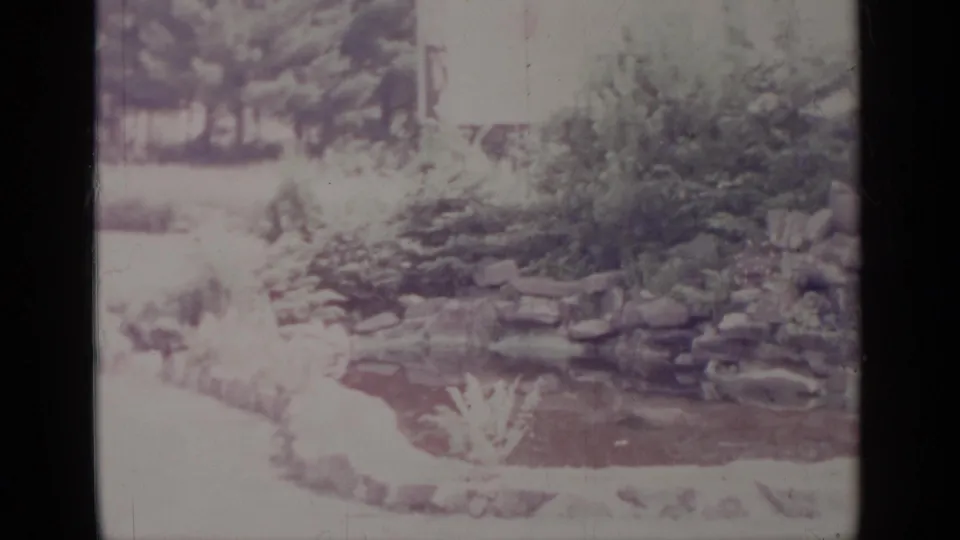1964 Greenwood Lake frame showing the garden pond from a similar angle, with stacked rocks and dense planting.