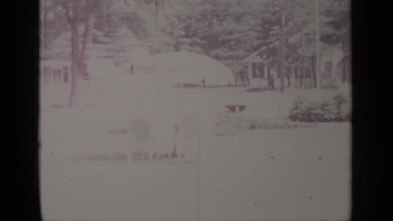 1964 Greenwood Lake winter frame with houses, trees, snow-covered ground, and a small yard feature seen through faded 8mm exposure.