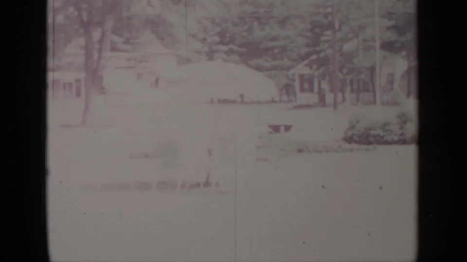 1964 Greenwood Lake winter frame with houses, trees, snow-covered ground, and a small yard feature seen through faded 8mm exposure.