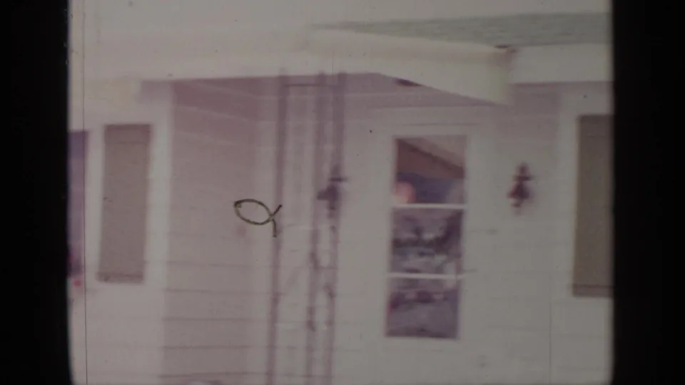 1964 Greenwood Lake home-movie frame showing a white house entry with a door, window, green shutters, and exterior wall light.
