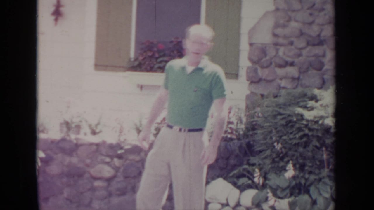 In Greenwood Lake, New York, a man in a green polo stands outside a white house with stone accents and flowers.