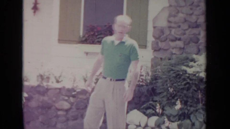 In Greenwood Lake, New York, a man in a green polo stands outside a white house with stone accents and flowers.