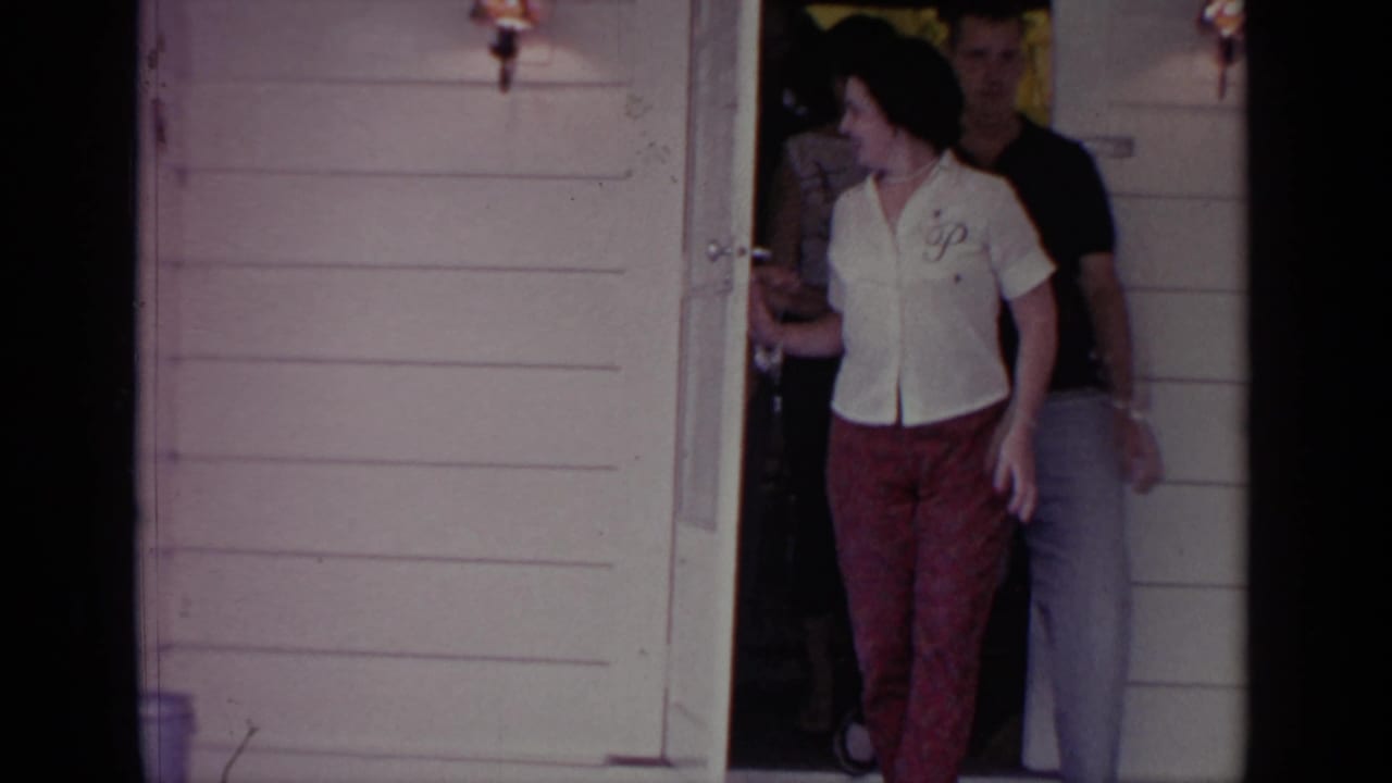 Adults begin leaving a light clapboard house through a front doorway.