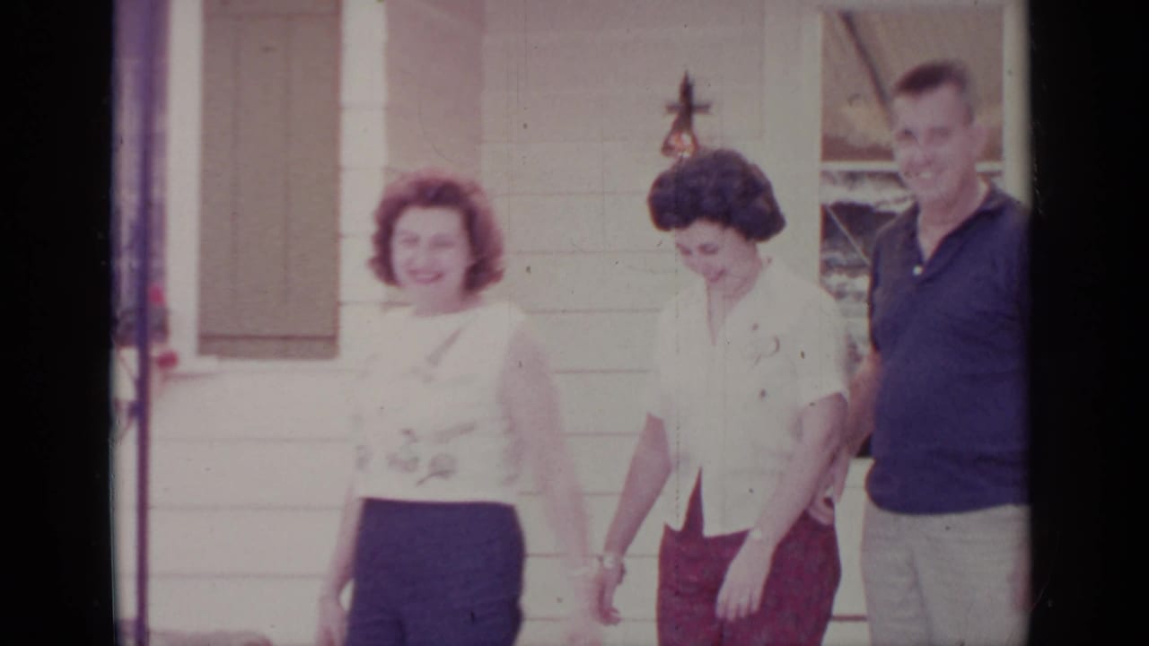 Adults outside a Greenwood Lake residence in 1964, with women in light blouses and a man near green shutters.