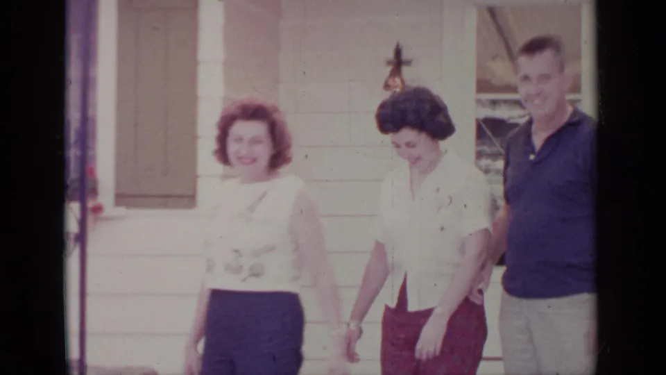 Adults outside a Greenwood Lake residence in 1964, with women in light blouses and a man near green shutters.