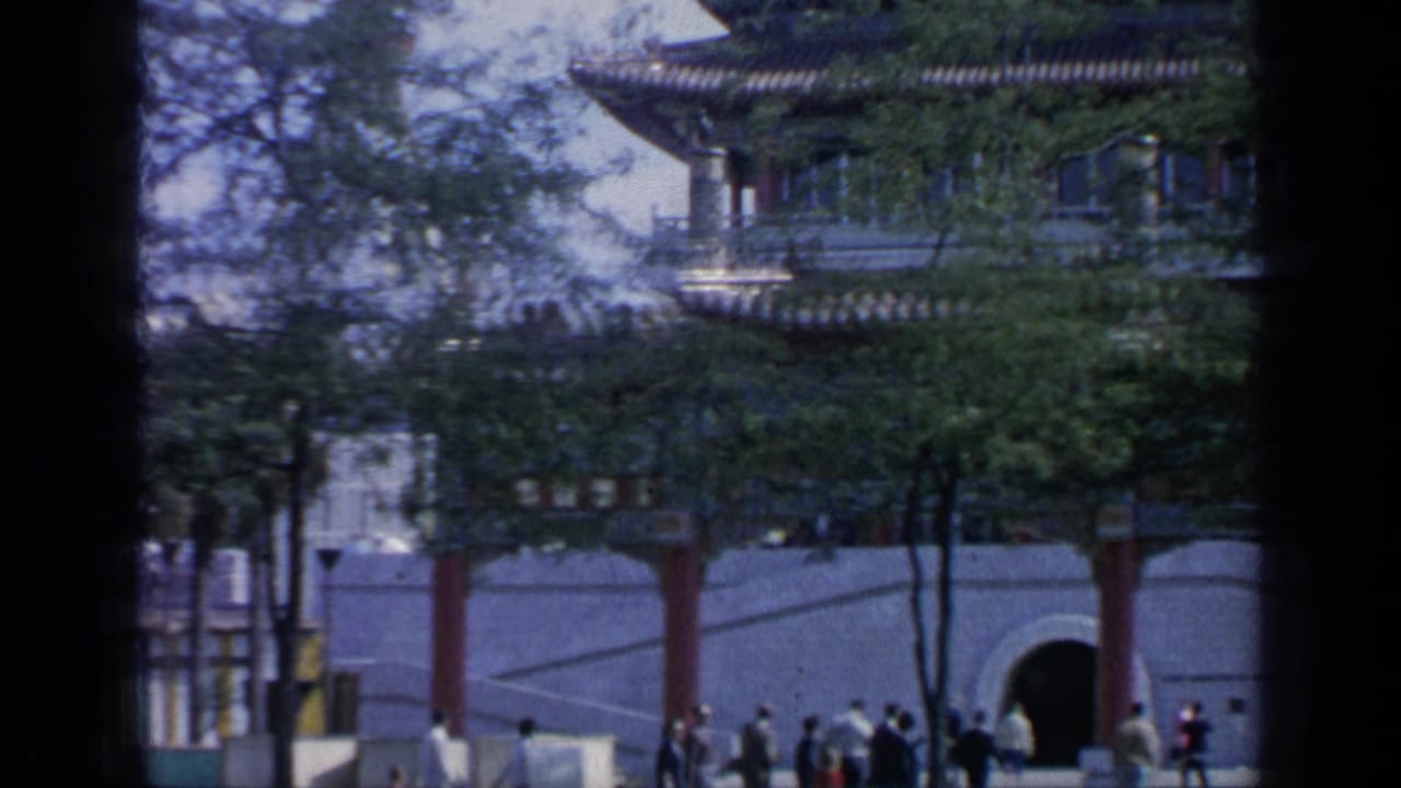 Chinese-style gate at Flushing Meadows with red columns, arched openings, trees, and visitors passing below.