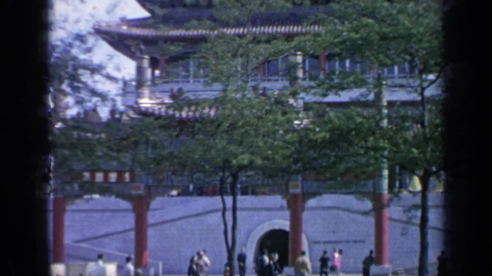 1964 fairground view of visitors near red columns, trees, and arched openings beneath a Chinese-style structure.