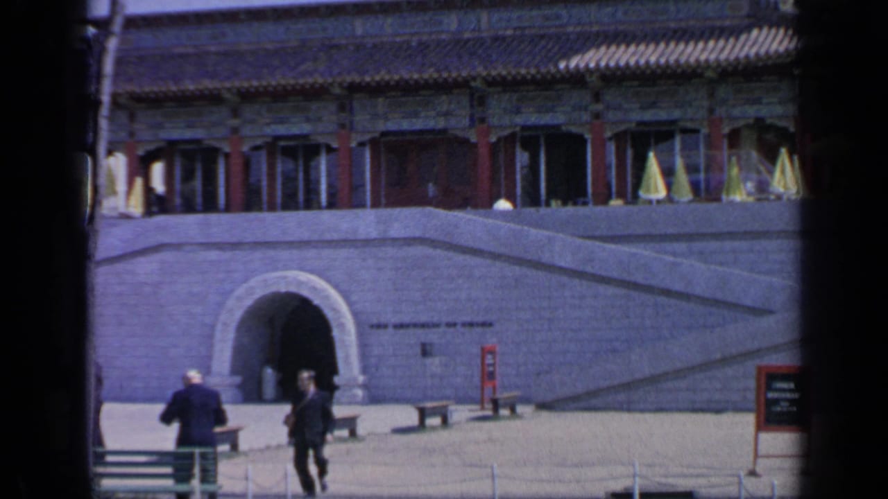 Visitors walk near a stone arched entrance beneath Chinese-style pavilion buildings.