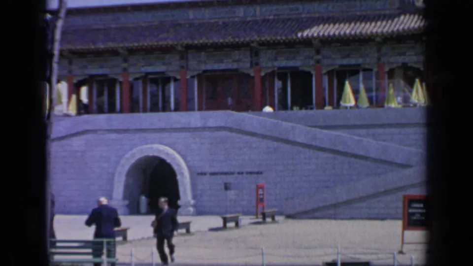 1964 Flushing Meadows home-movie frame showing visitors near an arched entrance below ornate Chinese-style pavilion architecture.