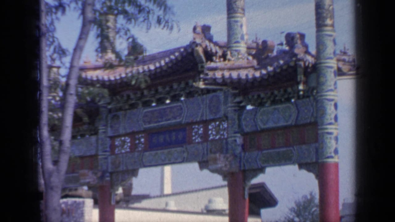 Decorated gateway roof and red columns are seen beside trees and pale walls.