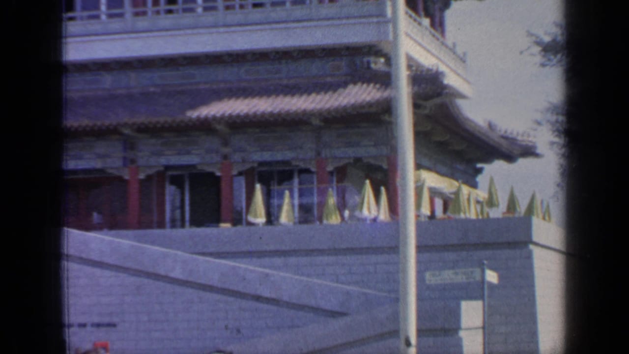 Traditional pavilion facade with tiled roof, terrace umbrellas, stonework, and a vertical pole.
