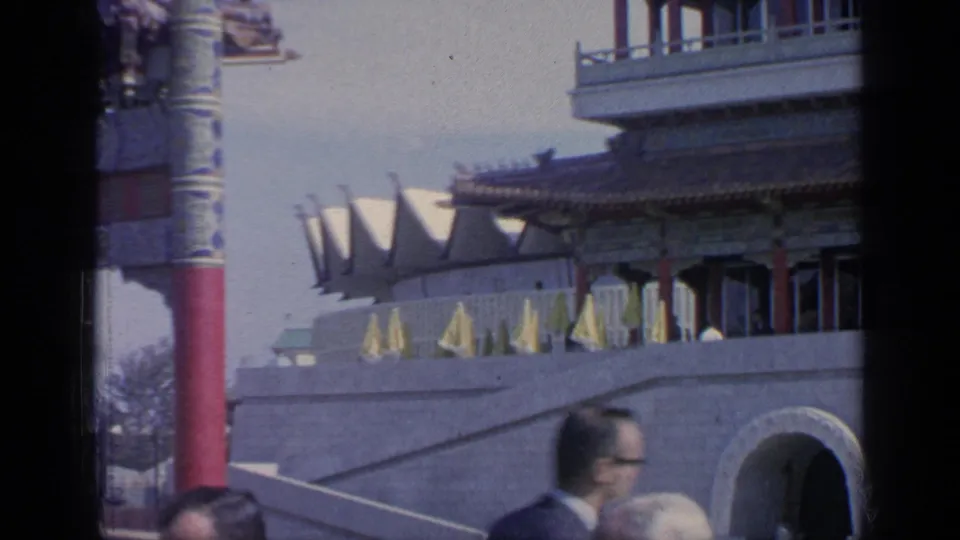 1964 Flushing Meadows World's Fair frame with pavilion architecture, terrace umbrellas, a stone arch, and fair visitors crossing the foreground.
