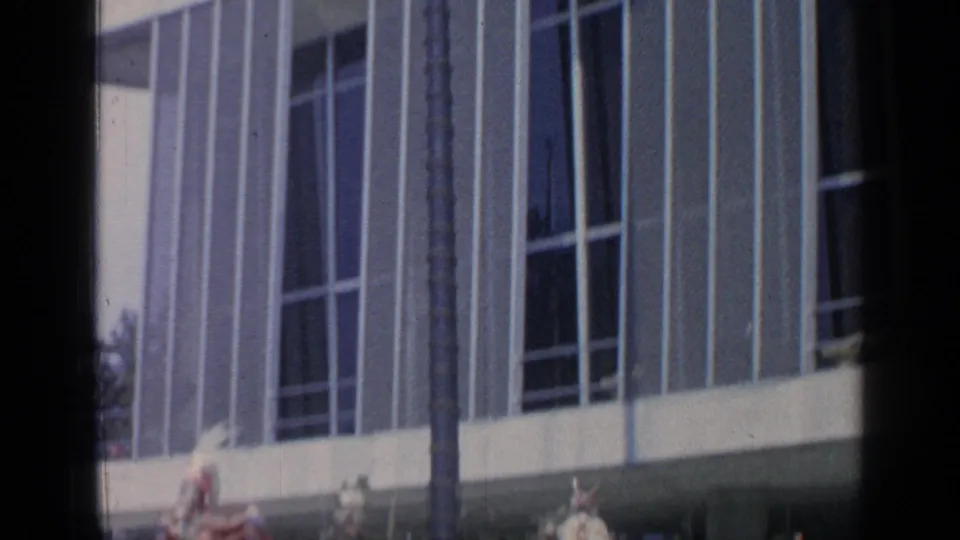 Handheld 8mm frame catches tall pavilion windows and partial costumed performers at the lower edge during the 1964 World's Fair scene.