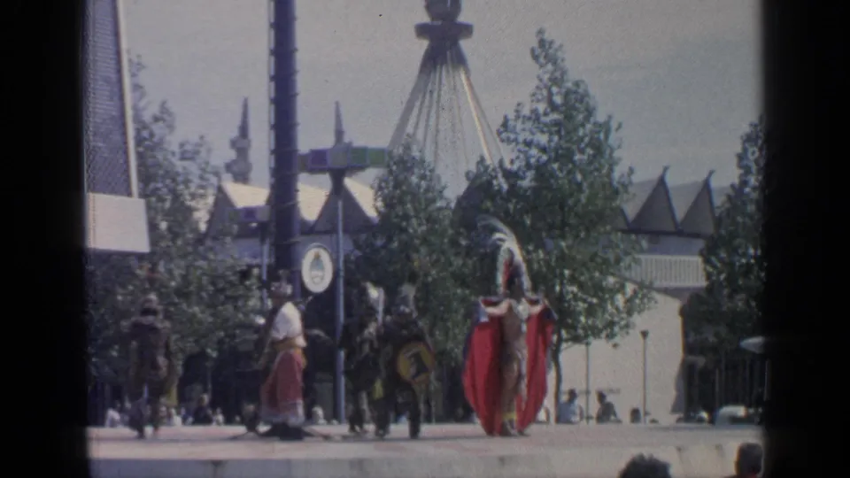 A red-caped dancer stands in a wide 1964 World's Fair view, with other performers, trees, signage posts, and pavilion roofs behind.