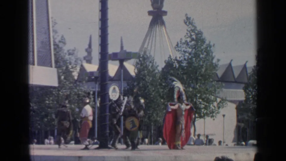 Visitor-shot 1964 World's Fair view in Flushing Meadows with a costumed figure near pavilion structures and passing fairgoers.