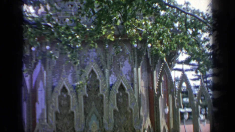 Home-movie frame showing Thailand Pavilion side arches, carved panels, hanging branches, and partial fairground background.