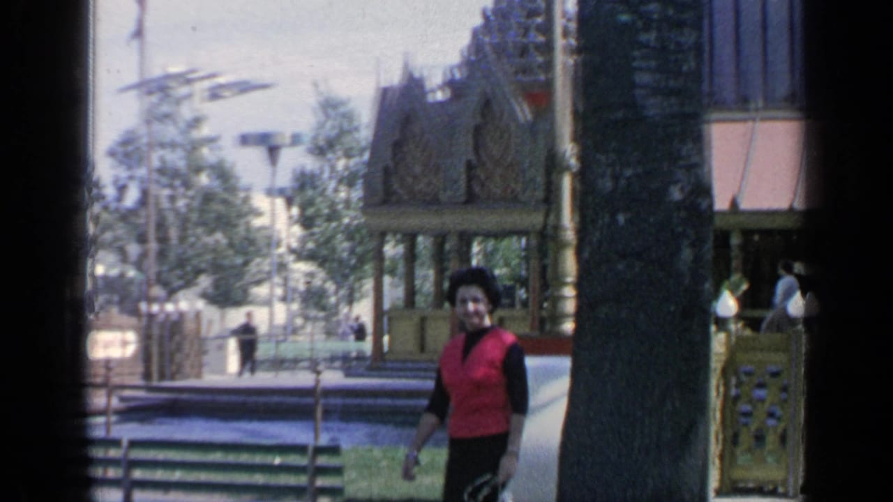 Woman in a red top walking near an ornate pavilion and trees.