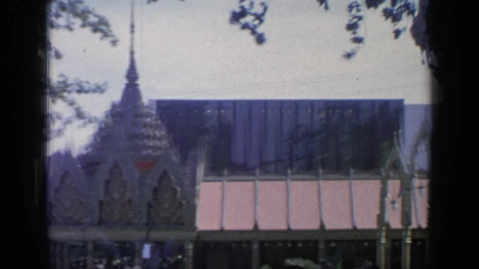 Fairground view at the 1964 New York World's Fair showing a modern exhibition building beyond Thai pavilion details and trees.