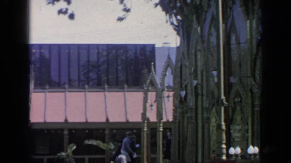 1964 Flushing Meadows fairground view with a modern building, trees, and part of the ornate Thai pavilion in the foreground.