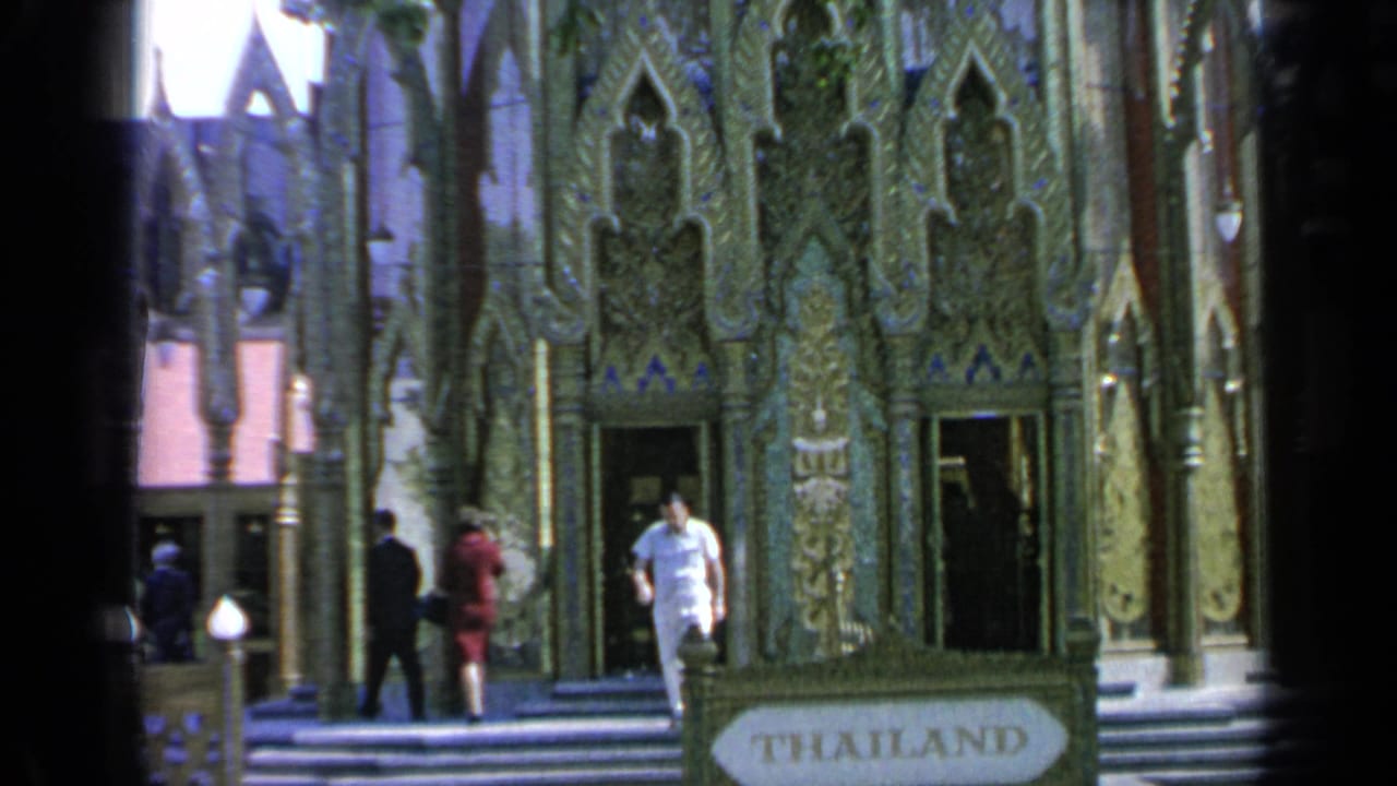 At the 1964 World's Fair in Flushing Meadows, a man in white descends the Thailand Pavilion steps as other visitors stand nearby.