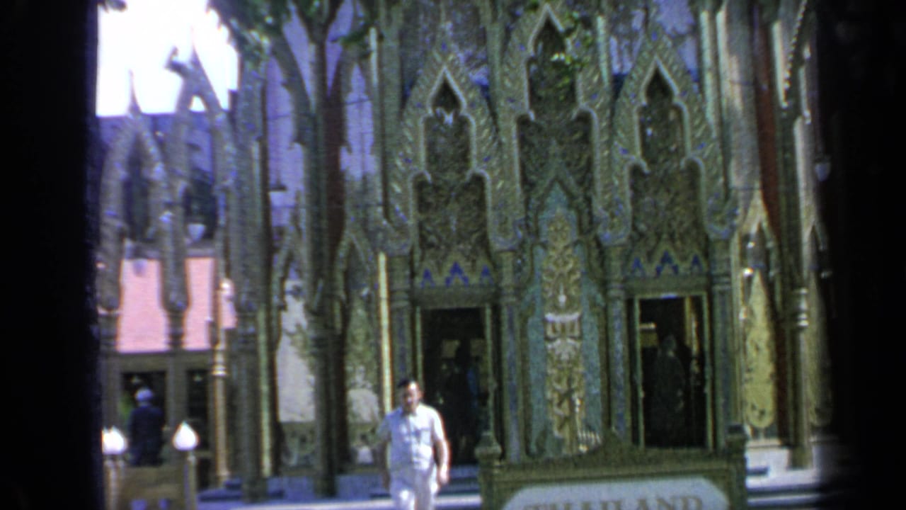 Man walks past ornate pavilion doors with the Thailand sign partly visible.
