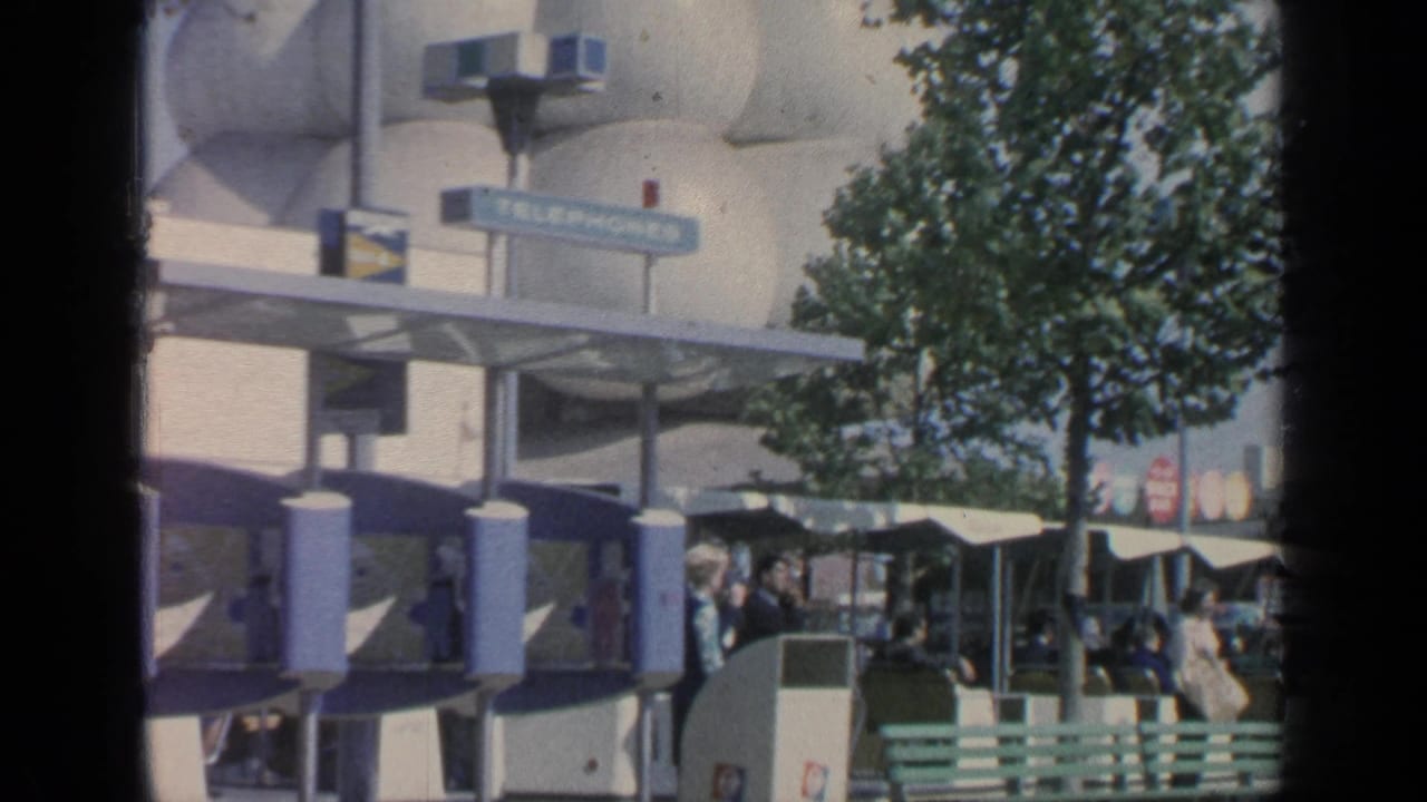 Flushing Meadows World's Fair visitors near green benches, a telephone booth, signage, trees, and a rounded white pavilion facade.
