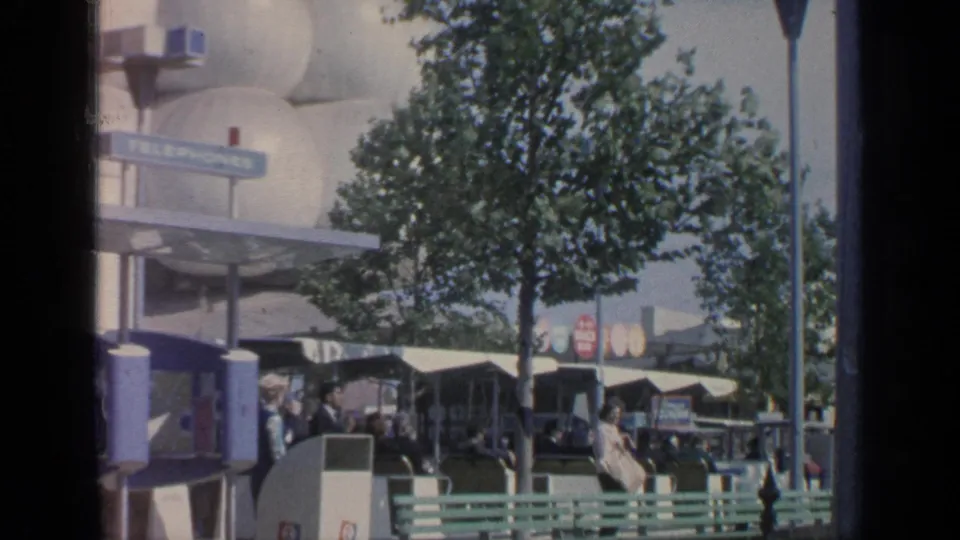 1964 World's Fair crowd scene at Flushing Meadows with benches, trees, canopies, and signage below a pale pavilion exterior.