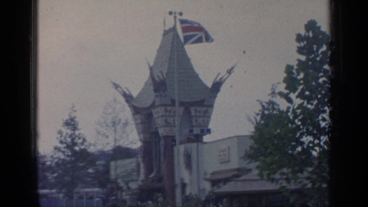 Pointed fair pavilion with a Union Jack flag, trees, and visitors below.