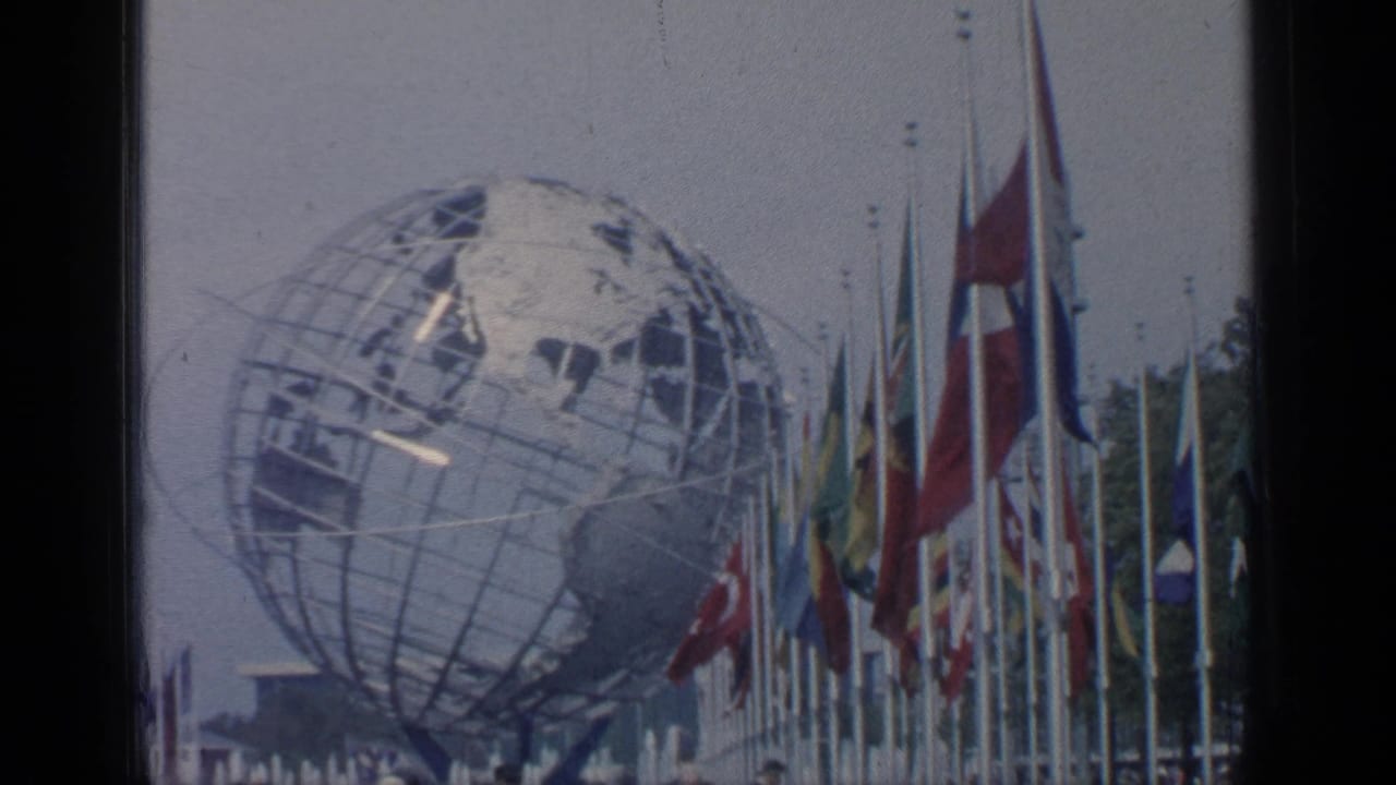 1964 Flushing Meadows view of the Unisphere with international flags and visitors partially visible below.