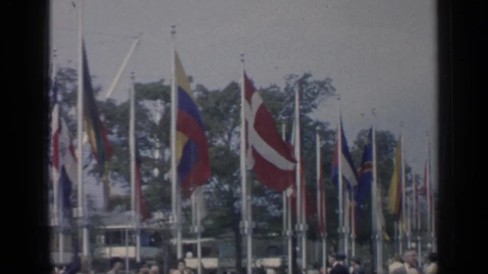 Rows of flags, including several recognizable national color patterns, stand above visitors at the 1964 New York World's Fair grounds.
