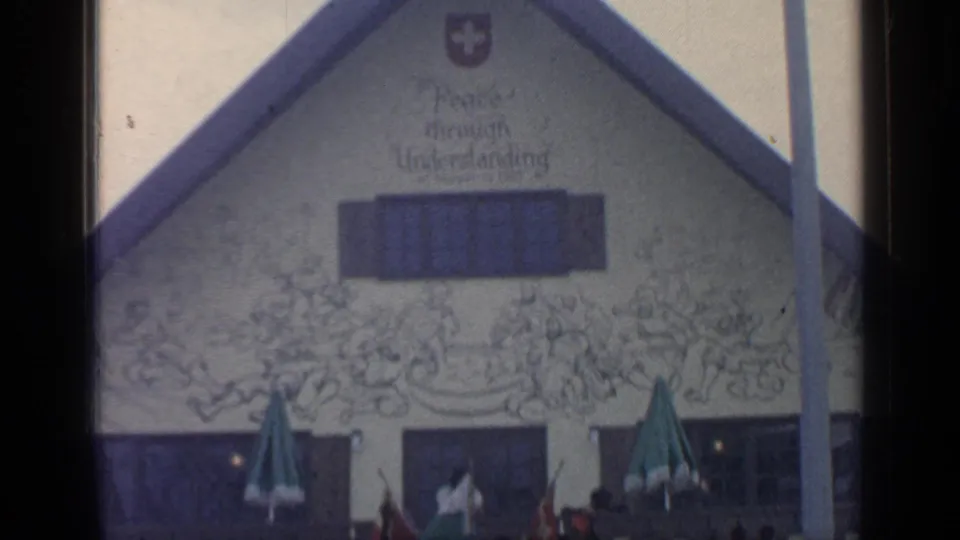 1964 Flushing Meadows World's Fair view of Le Chalet Restaurant facade with Swiss cross, mural text, green umbrellas, and visitors at street level.