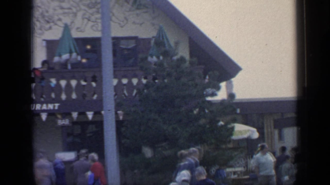 Restaurant balcony with green umbrellas, visitors, a tree, bunting, and partial restaurant sign.