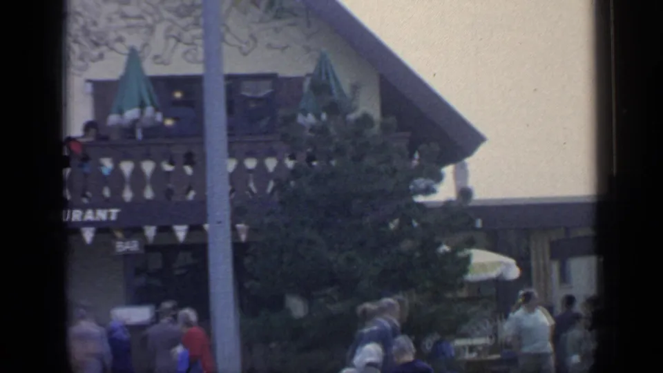 Le Chalet Restaurant balcony at the 1964 World's Fair, with visitors seated or standing near green umbrellas and bunting above the entrance.