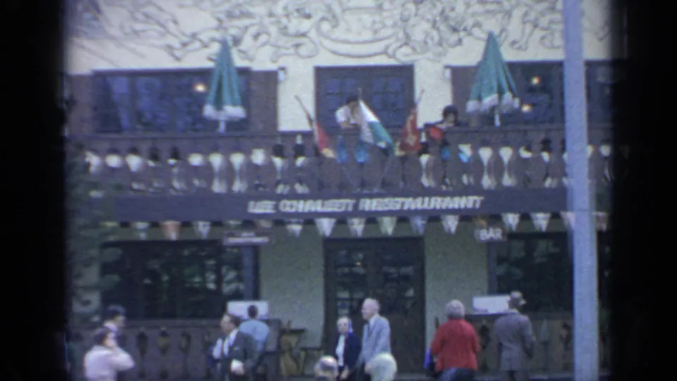 1964 World's Fair restaurant exterior with Le Chalet Restaurant lettering, balcony bunting, green umbrellas, bar signs, mural detail, and visitors outside.
