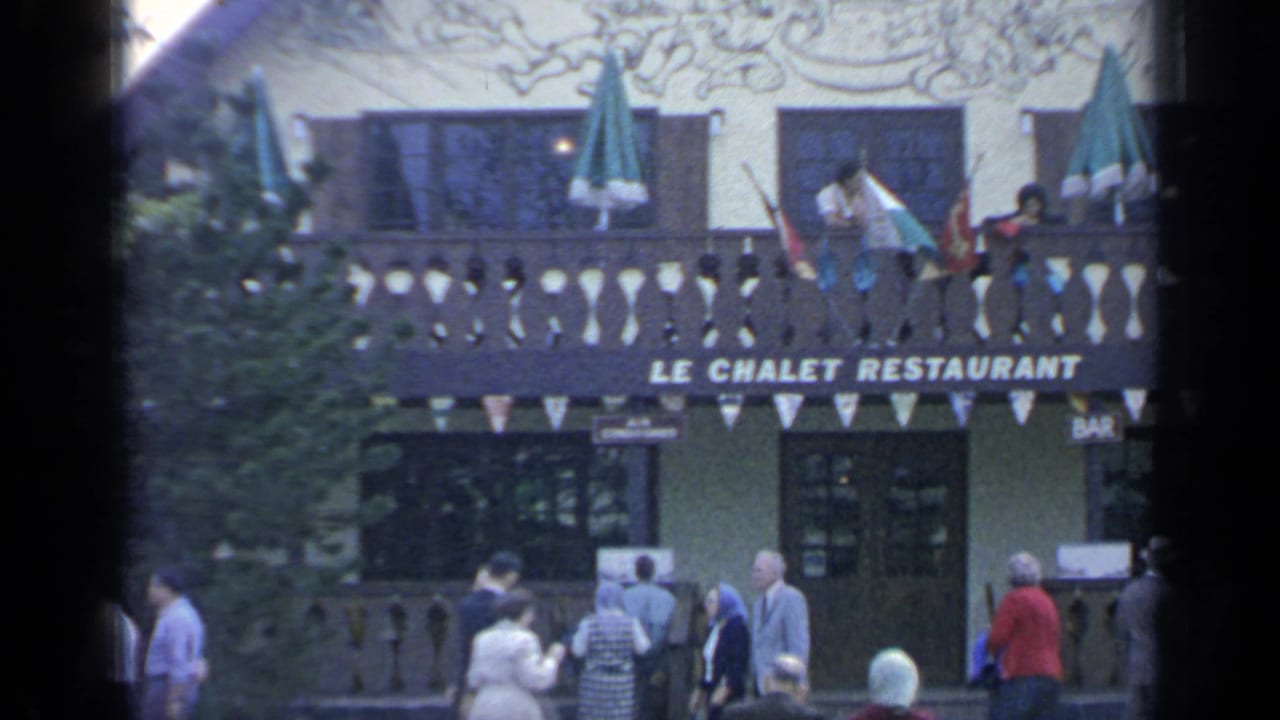 Visitors walk below the Le Chalet Restaurant balcony with umbrellas and bunting.