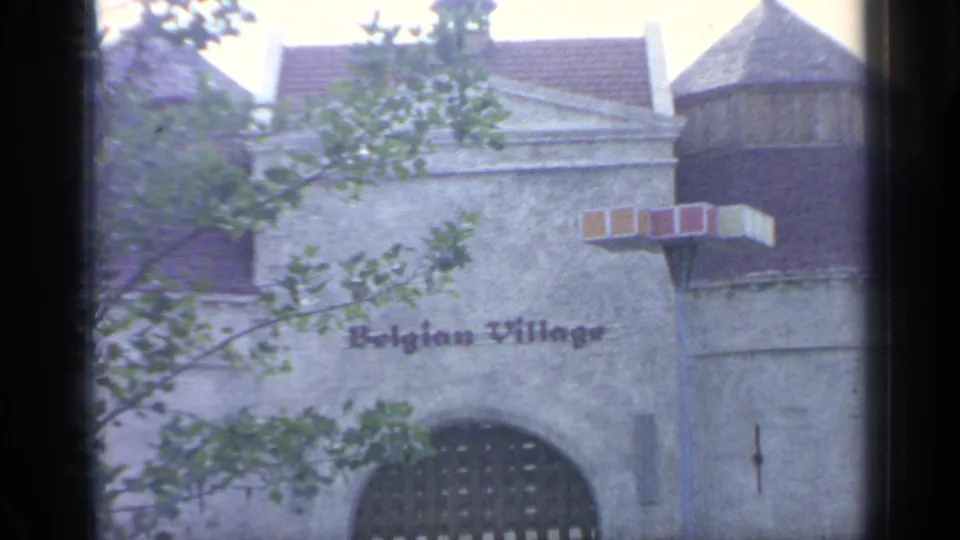 The Belgian Village entrance at the 1964 New York World's Fair appears with lettering on a textured wall, trees, rooflines, and an arched gate.