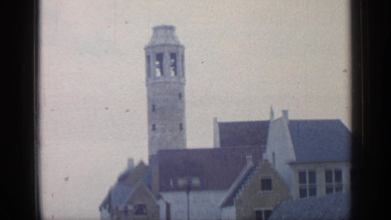 Bell tower and gabled Belgian-style buildings seen through a dark window frame.