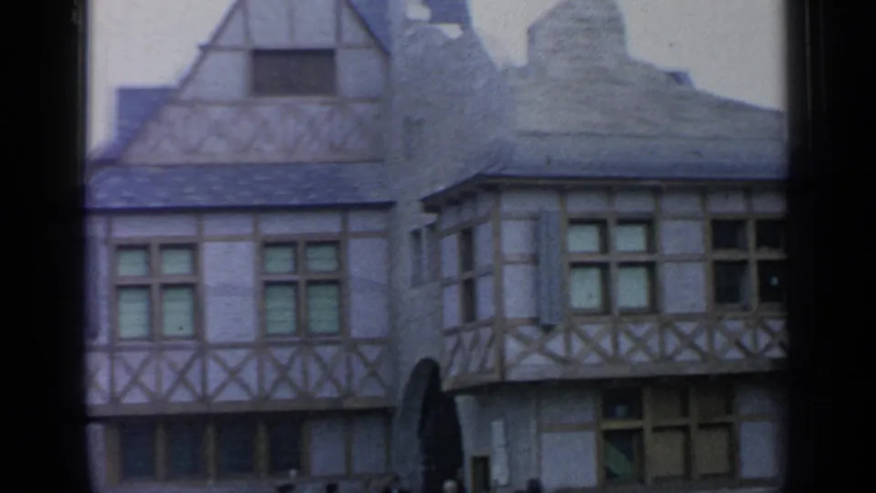 Belgian Village timber-framed buildings with multi-pane windows and stone details, recorded from a windowed vantage point in 1964.