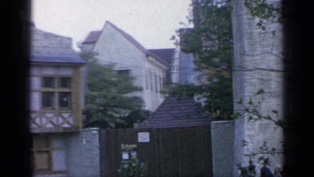 Upper portions of Belgian-style buildings, fencing, trees, and partial fair signage.