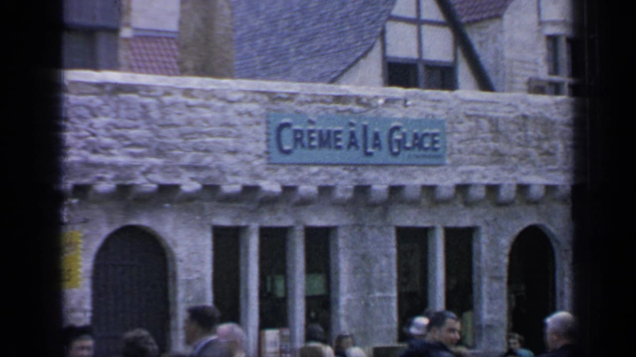 Crème à la Glace signage on a stone fairground building at Flushing Meadows, with visitors moving across the foreground.