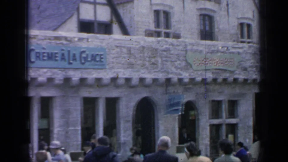 1964 fairground street view with the Crème à la Glace sign, adjacent storefront signage, arched doorway, and visitors in period dress.