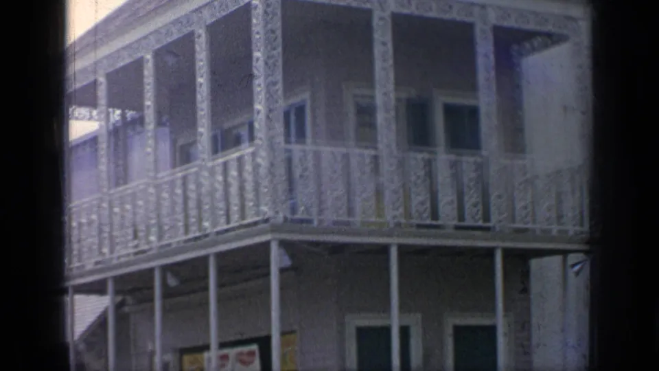 1964 Flushing Meadows fairground building with ornate balcony railings, shaded windows, posts, and decorated storefront signs below.