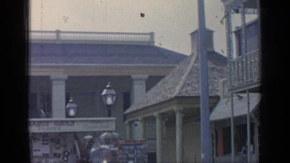 1964 Flushing Meadows frame showing the Mardi Gras Shoppe sign, lampposts, rooflines, souvenir racks, and visitors in soft 8mm color.