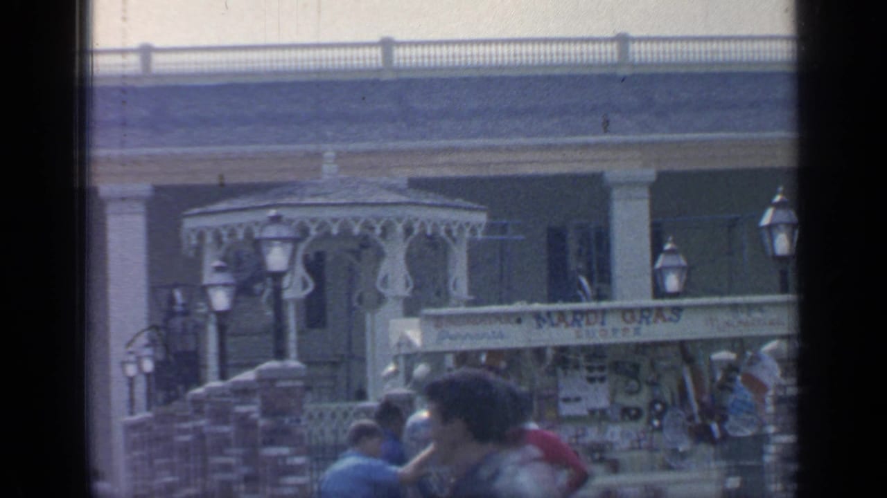 Tourists move past lampposts and a souvenir shop in front of a large building.